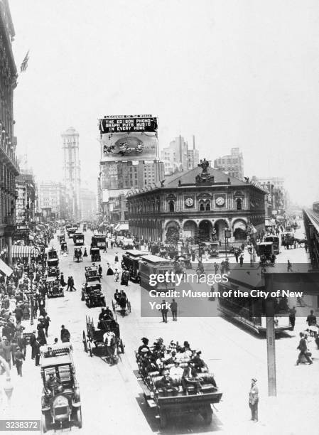 Aerial view of crowds, streetcars and carriages traveling down Broadway at Herald Square, looking North from 34th Street, New York City. A billboard...