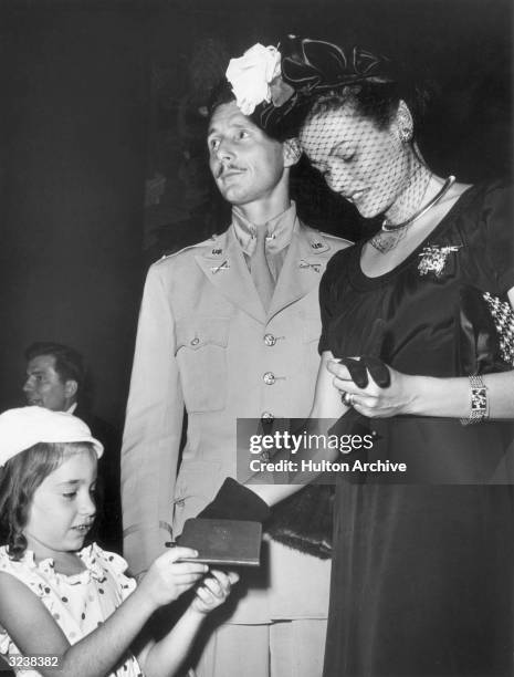 American actor Gene Tierney signs an autograph for a young girl as her husband, French-born fashion designer Oleg Cassini, looks on. Tierney wears a...