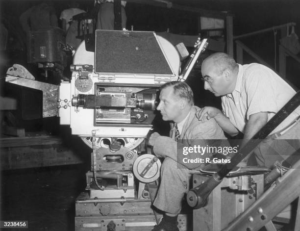 Profile view of American film director Norman Taurog , explaining the motion picture camera to atomic expert Dr Henry T Wensel, who was on leave from...