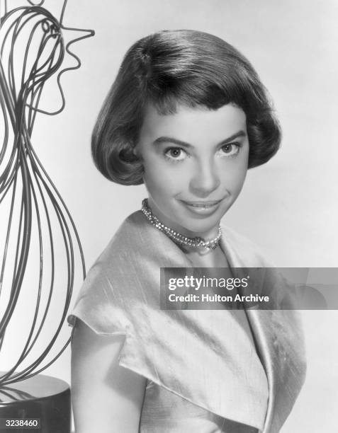 Headshot portrait of French-born actor and dancer Leslie Caron wearing a raw silk dress with oversized lapels and a pearl choker, with a sculpture in...