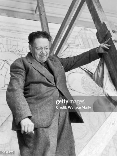 Low-angle view of Mexican artist Diego Rivera standing on scaffolding while working on a mural entitled, 'The Great City of Tenochtitlan,' National...