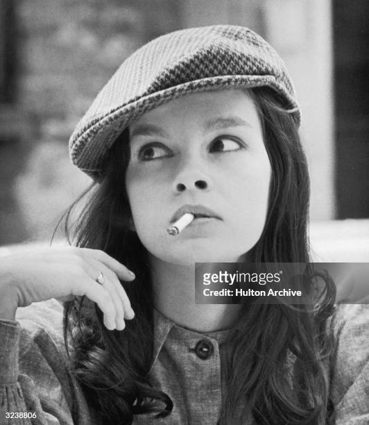 Headshot of French-Canadian actor Genevieve Bujold, wearing a herringbone cap, smoking a cigarette and looking to the side.