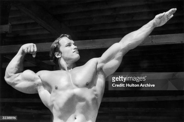 Austrian-born bodybuilder Arnold Schwarzenegger points one hand out as he flexes his torso on Muscle Beach, Santa Monica, California.
