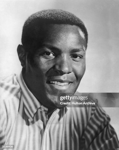 Studio portrait of American decathlete Rafer Johnson, two-time Olympic medal winner, smiling and wearing a striped shirt.