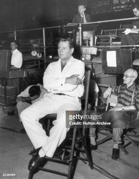Cuban-born actor and bandleader Desi Arnaz holds a cigarette while sitting on the set of a television program.