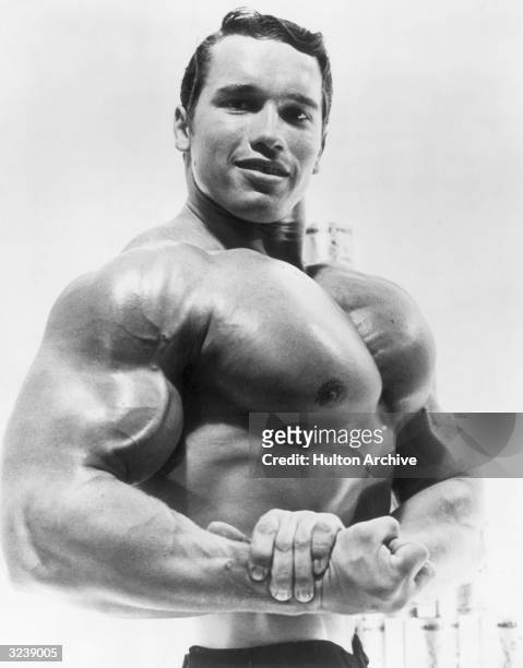 Studio portrait of Austrian-born bodybuilder Arnold Schwarzenegger flexing his torso in an advertisement for a German protein product.