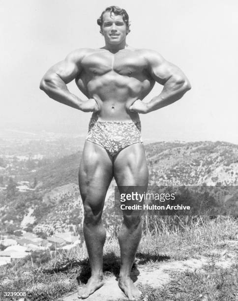 Full-length image of Austrian-born bodybuilder Arnold Schwarzenegger standing and flexing on top of a hillside near Muscle Beach, Santa Monica,...