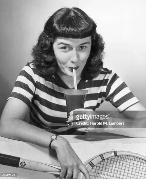 Woman holding a tennis racket sips a drink through a straw.