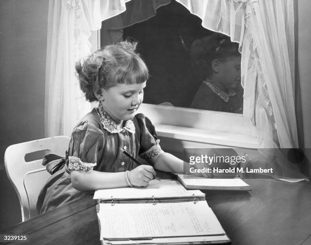 An elementary school girl writes the answers to her homework assignment in a loose-leaf notebook.