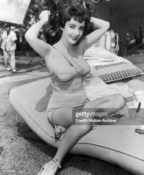 Full-length image of British-born actor Elizabeth Taylor combing her hair in a bathing suit on the set of director Richard Thorpe's film, 'The Girl...