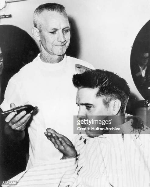 American singer and actor Elvis Presley blows a strand of hair from his hand, while receiving a haircut from a US Army barber, Fort Chaffee,...