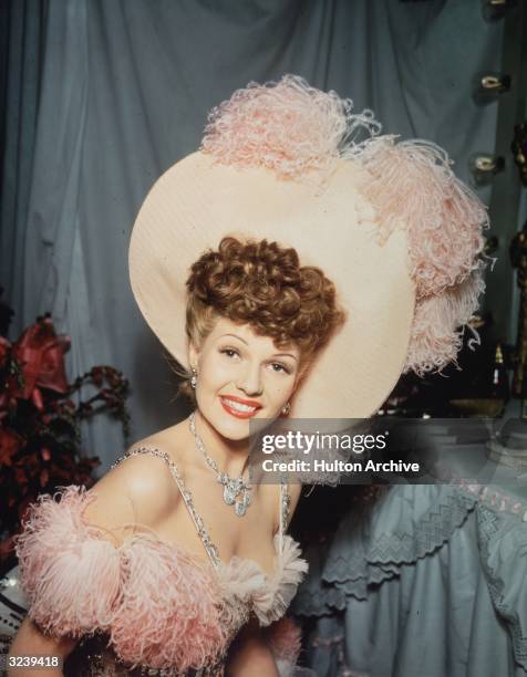 American actor Rita Hayworth smiles while wearing an 1890s showgirl costume trimmed with ostrich feathers, in a promotional portrait for director...