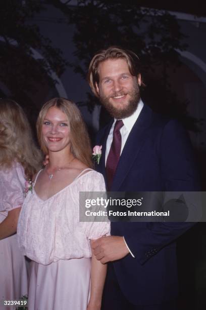 American actor Jeff Bridges and his wife, Susan Geston, smiling while at a formal event. Bridges is wearing a navy blue suit and has a beard. Geston...