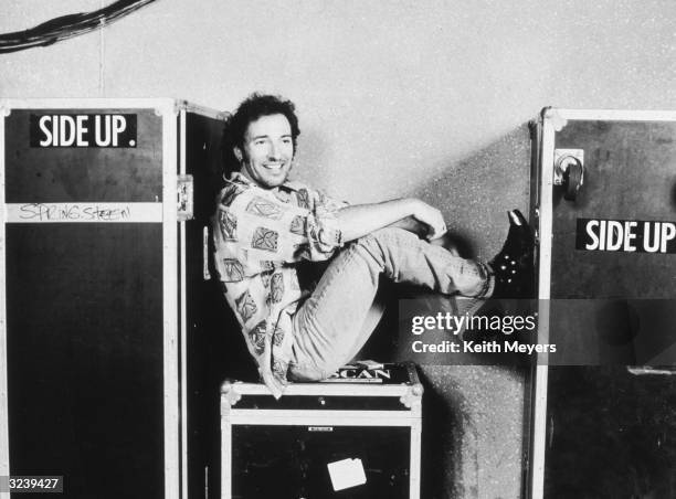American musician Bruce Springsteen sits on a trunk with his feet up backstage at the Brendan Byrne Arena in the Meadowlands sports complex, East...