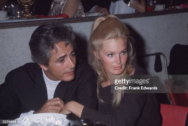 Married American actors John Derek and Linda Evans sit together in close proximity during an Emmy Awards ceremony. Evans wears her long blonde hair...