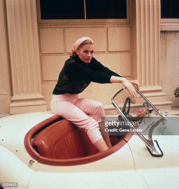 Portrait of Swedish actor Anita Ekberg sitting on the trunk of a cream convertible with her feet in its red leather interior, Hollywood, California....