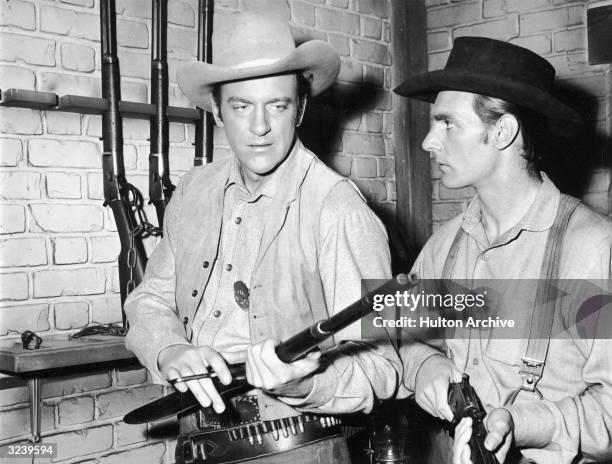 Actors James Arness , as Marshall Matt Dillon, and Dennis Weaver inspect rifles from a rack, in a still from the television series 'Gunsmoke'.