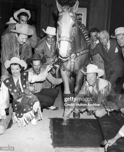 American actor and singer Roy Rogers helps his horse Trigger make a hoof print in the cement as his wife Dale Evans holds the horse's bridle, during...