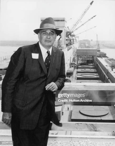 New York City parks commissioner Robert Moses stands and leans on a wooden railing in front of a waterfront project site, New York City. Winches are...