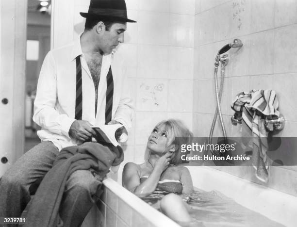 French actor Michel Piccoli sits on the edge of a tub while French actor Brigitte Bardot takes a bath in a still from director Jean-Luc Godard's...