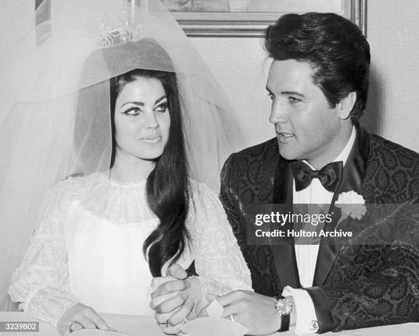 American rock n' roll singer and actor Elvis Presley sits and holds hands with his bride Priscilla Presley on their wedding day, Las Vegas, Nevada....