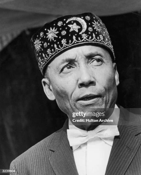 Headshot of American religious leader Elijah Muhammad , leader of the Black Muslims, wearing a black cap embroidered with the crescent and star...