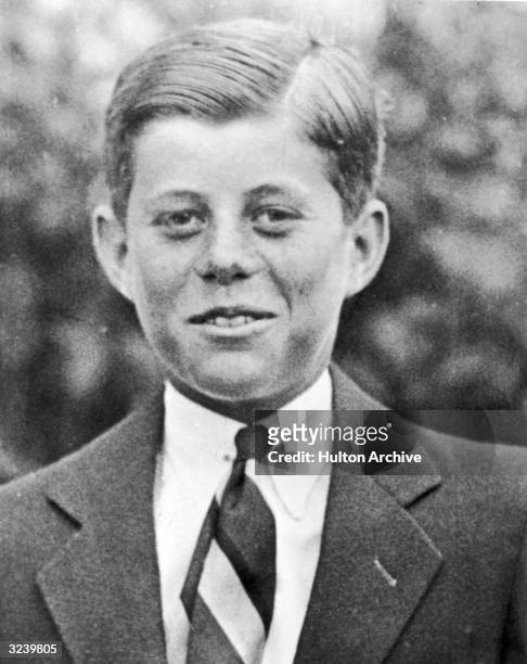Headshot portrait of John F Kennedy at age ten, standing outdoors and wearing a suit with his hair slicked back.