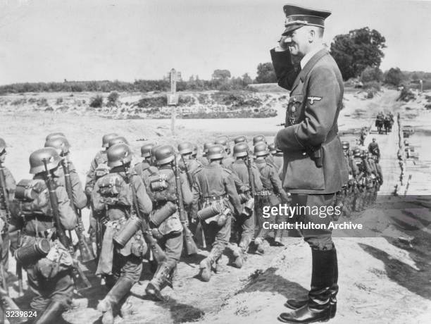 German Fuhrer Adolf Hitler salutes as he oversees his military troop during the Nazi occupation of Poland. The troops march in formation toward a...