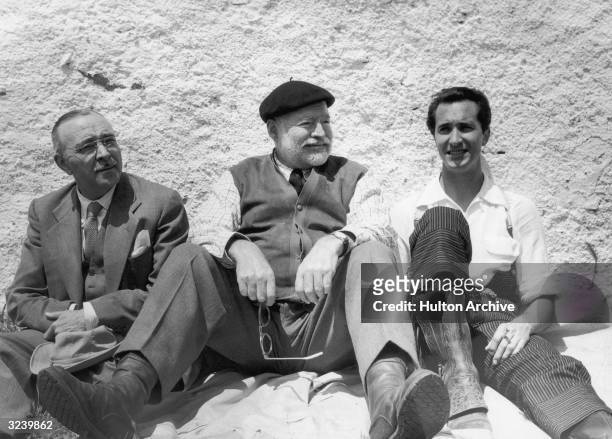American author Ernest Hemingway , and Spanish bullfighter Luis Dominguin , smoking a cigarette, sit against a wall, Spain.