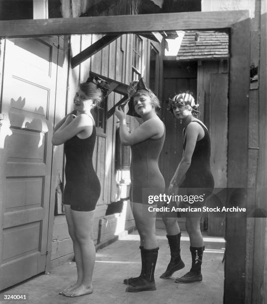 Three of Mack Sennett's Bathing Beauties stand in a row in their one-piece bathing suits, two of them wearing shoes and socks.