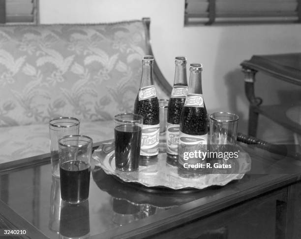 Still life of three 12 ounce bottles of Pepsi Cola arranged with glasses on a silver platter