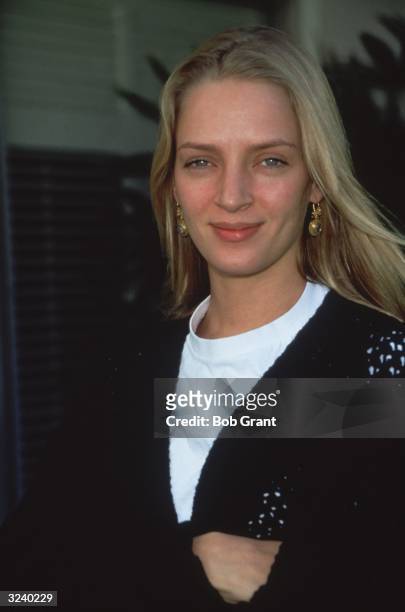 American actor Uma Thurman, wearing a white t-shirt and a black sweater, smiling outdoors.