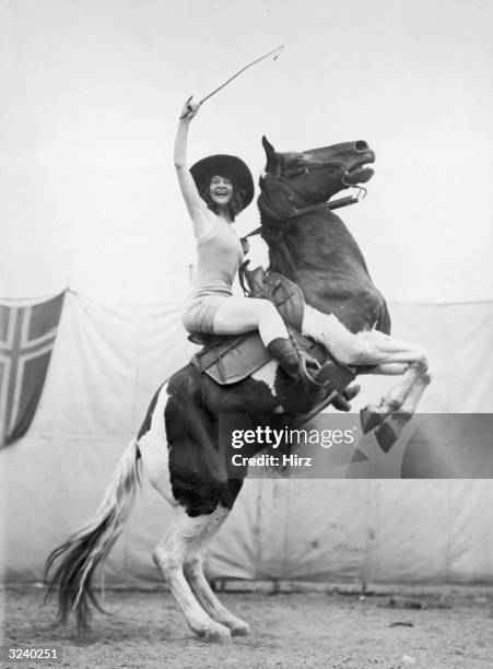 Full-length portrait of rodeo champion and actor Betty Miles on a horse bucking up on its hind legs.