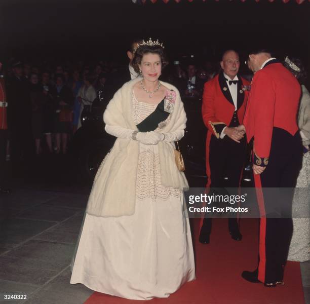 Queen Elizabeth II attends a film premiere wearing a white beaded evening gown by designer Norman Hartnell.