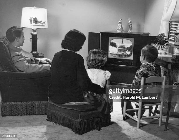 Couple and their daughter and son gather around a television set, upon which is an image of the Capitol Dome in Washington D.C.