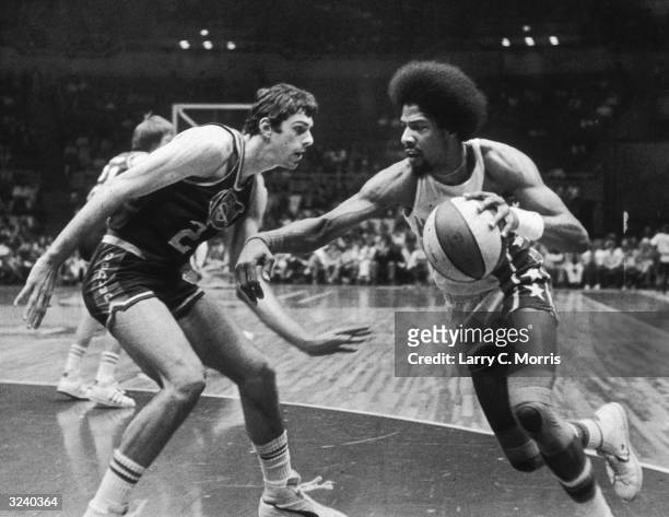 American basketball player Julius Erving of the New Jersey Nets, nicknamed 'Dr J,' driving past Bobby Jones of the Denver Nuggets during a game.