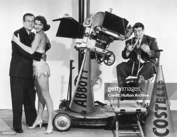 Promotional portrait of American comedy team Bud Abbott and Lou Costello clowning on a film set with a young woman, a movie camera, a tape measure,...