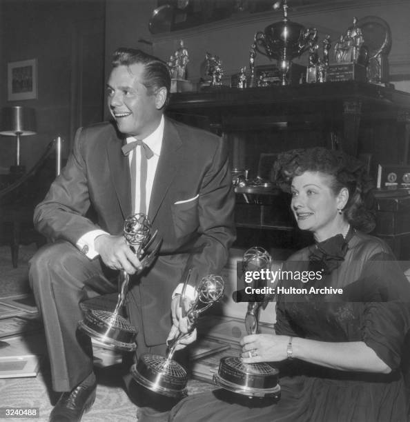 American actor and comedian Lucille Ball and her husband, Cuban-born actor Desi Arnaz smile in front of a trophy case, holding three of their Emmy...