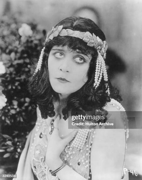 American actor Theda Bara looks up, holding one hand to her chest in a still from director J. Gordon Edwards' silent film 'Salome'. She wears a...