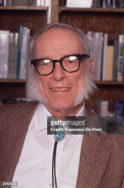 Russian-born American author Isaac Asimov smiling while posing in front of a bookcase.