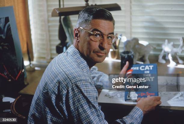 American author and illustrator Dr Seuss sits at his drafting table in his home office with a copy of his book, 'The Cat in the Hat', La Jolla,...