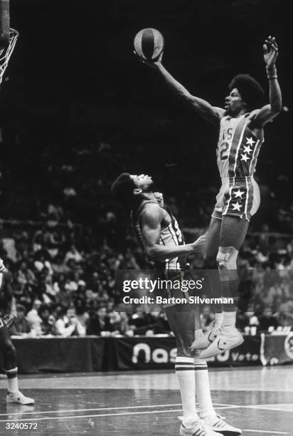American basketball player Julius Erving, nicknamed 'Dr J,' of the New Jersey Nets leaping high over Len Elmore of the Indiana Pacers for a score.