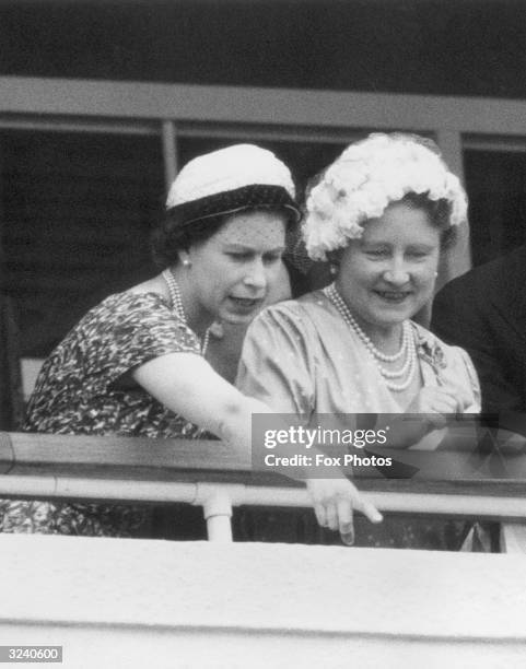 Queen Elizabeth II pointing something out to Queen Elizabeth the Queen Mother during Ladies Day at Ascot.