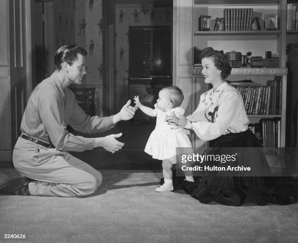 Married American actors Shirley Temple and John Agar play with their infant daughter, Linda Susan, in the living room of their home.