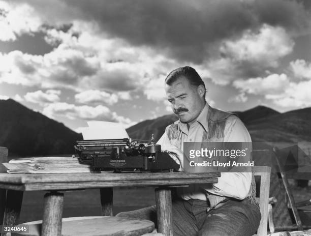 American writer Ernest Hemingway works at his typewriter while sitting outdoors, Idaho. Hemingway disapproved of this photograph saying, 'I don't...