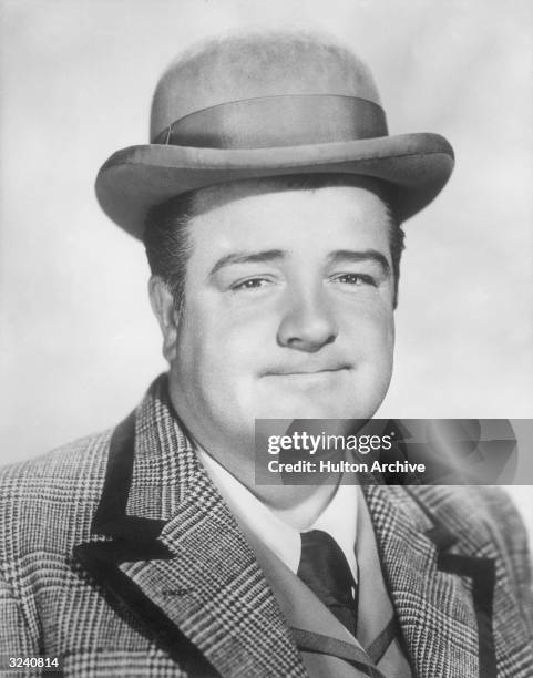 Studio headshot portrait of American actor and comedian Lou Costello grinning, wearing a bowler hat and a tweed sport coat.