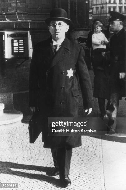 Full-length view of a middle class German Jew walking with a briefcase in Berlin, Nazi Germany. He wears a Star of David on the overcoat of his...