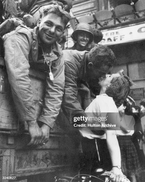 An American soldier leans over the side of an army vehicle as he kisses a French woman on a bicycle during the liberation of Paris. Other soldiers...