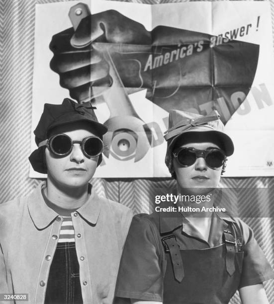 Propaganda image of two female factory workers, wearing wearing goggles, caps, and aprons, posing in front of a poster for the American homefront war...