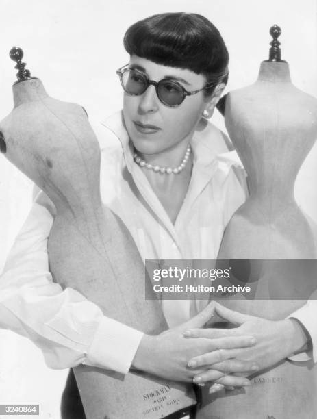 Portrait of American costume designer Edith Head embracing two miniature dressmaker dummies.